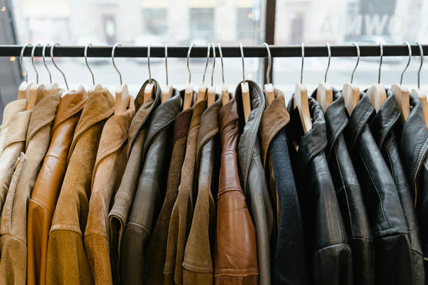 A clothing rack displaying assorted leather jackets in brown and black tones hanging on wooden hangers inside a retail store.